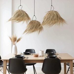 Three handwoven palm leaf pendant lights clustered above minimalist dining table with black chairs