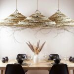 Three oversized palm leaf pendant lights with natural woven tiers hanging above modern dining table setting