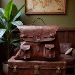 Brown leather messenger bag displayed upright on vintage trunk in rustic interior with world map decor