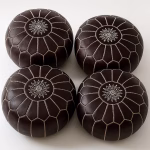 Set of four dark-brown leather pouffe ottoman pieces with white embroidery, viewed from above.