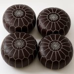 Four dark brown leather floor ottomans with white embroidered stars and geometric stitching pattern arranged together