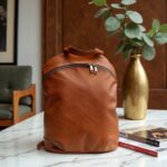 Brown leather backpack purse on marble table with books, premium full-grain leather laptop bag