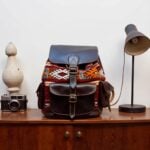 Dark brown leather kilim backpack with geometric patterns styled on wooden desk with camera and lamp