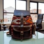 Dark brown leather kilim backpack with geometric handwoven patterns placed on table in modern office interior