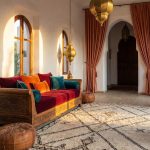 Moroccan-style living room with colorful cushions, geometric Berber rug, brass lanterns, leather pouf, and traditional zellige tile accents