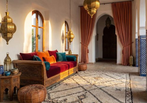 Moroccan-style living room with colorful cushions, geometric Berber rug, brass lanterns, leather pouf, and traditional zellige tile accents