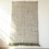Green Moroccan rug with handwoven geometric patterns and fringed edges on white wall