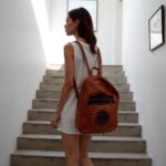 Woman on stairs with handmade leather backpack featuring circular sun embossing in rich cognac tone