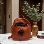 Full-grain leather backpack handmade with embossed sun rosette next to eucalyptus in elegant interior
