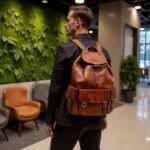 Professional wearing brown leather buckle backpack in modern office, showing full-grain leather craftsmanship