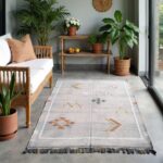 Gray cactus rug with tribal motifs displayed on covered patio with plants and natural wood furniture