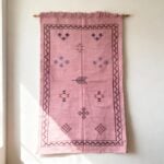 Pink Moroccan rug with tribal embroidery hanging on wall - handwoven cactus silk tapestry with fringe