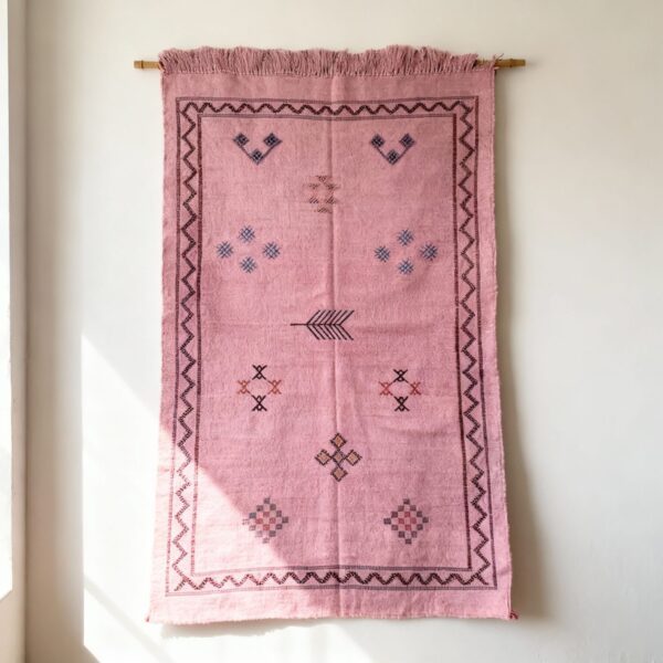 Pink Moroccan rug with tribal embroidery hanging on wall - handwoven cactus silk tapestry with fringe