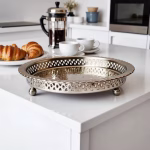Elegant hammered silver circle tray with openwork border holding breakfast croissants on kitchen counter