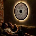 Backlit round brass wall light displaying intricate geometric perforations in warm intimate setting