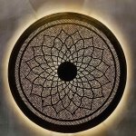 Illuminated round brass wall light creating mesmerizing shadow patterns through hand-pierced metalwork on wall