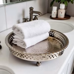 Hand hammered silver circle tray with perforated rim holding rolled white towels in bathroom