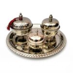 A professional studio shot of a hand hammered silver tea set featuring three footed containers with a dimpled texture on a matching round tray, isolated on a white background.