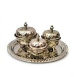 A professional studio shot of a three-piece silver tea container set with ornate lids on a matching silver tray, isolated on a white background.