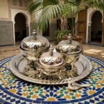 Ornate silver tea container set resting on a blue and yellow zellige mosaic table in a Riad courtyard