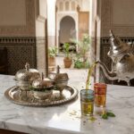 Silver tea container set on marble next to Moroccan tea glasses and traditional mint tea pouring