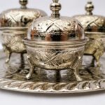 Close-up of hand-engraved floral patterns and curved legs on a silver tea container set