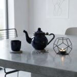 Deep blue moroccan enamel teapot stovetop on grey surface with matching cup and loose tea leaves