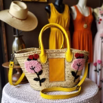 Embroidered straw bag with yellow leather handles displayed with summer fashion