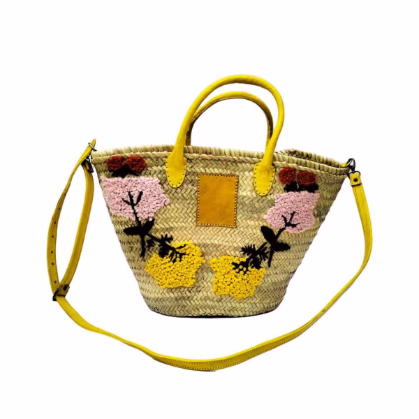 Front view of embroidered straw bag with yellow leather trim and shoulder strap