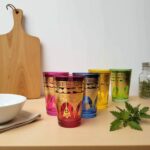 Amber and purple golden henna tea glasses on a wooden board next to a white bowl