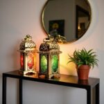 Engraved brass candle holders glowing on black console table with green and red glass creating warm ambiance