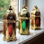 Three engraved brass candle holders on windowsill showing detailed metalwork and red, amber, green glass panels