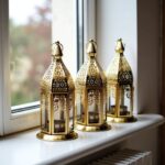 Three engraved brass candle holders with transparent glass panels displayed on windowsill in natural light