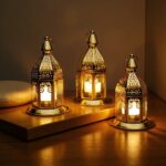 Engraved brass candle holders in varying sizes glowing with candlelight on wooden table surface