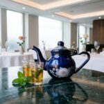Blue floral enamel teapot on green marble table with Moroccan tea glasses in a sunlit dining area