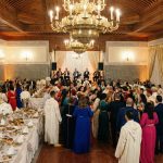 A grand, festive Moroccan wedding hall featuring intricate wall tiles, large brass chandeliers, and elegantly decorated tables in a warm, golden-lit setting.