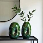 Pair of emerald green sculptural ceramic vases with organic dimpled texture on black shelf