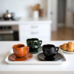 Three ceramic coffee cups with saucers on white tray, featuring artisan-crafted raised swirl patterns in bold colors
