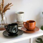 Small ceramic coffee cups in terracotta and dark green with glossy finish and decorative handle details
