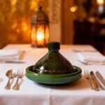 Authentic ceramic tagine pot on elegant dining table with lantern, traditional Moroccan serving cookware