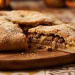 Sliced Moroccan Berber pizza on a wooden board showing the seasoned ground lamb and onion filling inside the golden crust