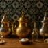 Three Moroccan teapots in silver brass and stainless steel with cleaning supplies on traditional tile background