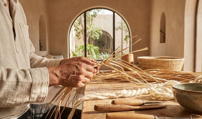 A close-up photograph of an artisan’s hands weaving natural fibers in a bright, modern studio, surrounded by sustainable handmade Moroccan pottery and textiles, symbolizing the preservation of tradition.