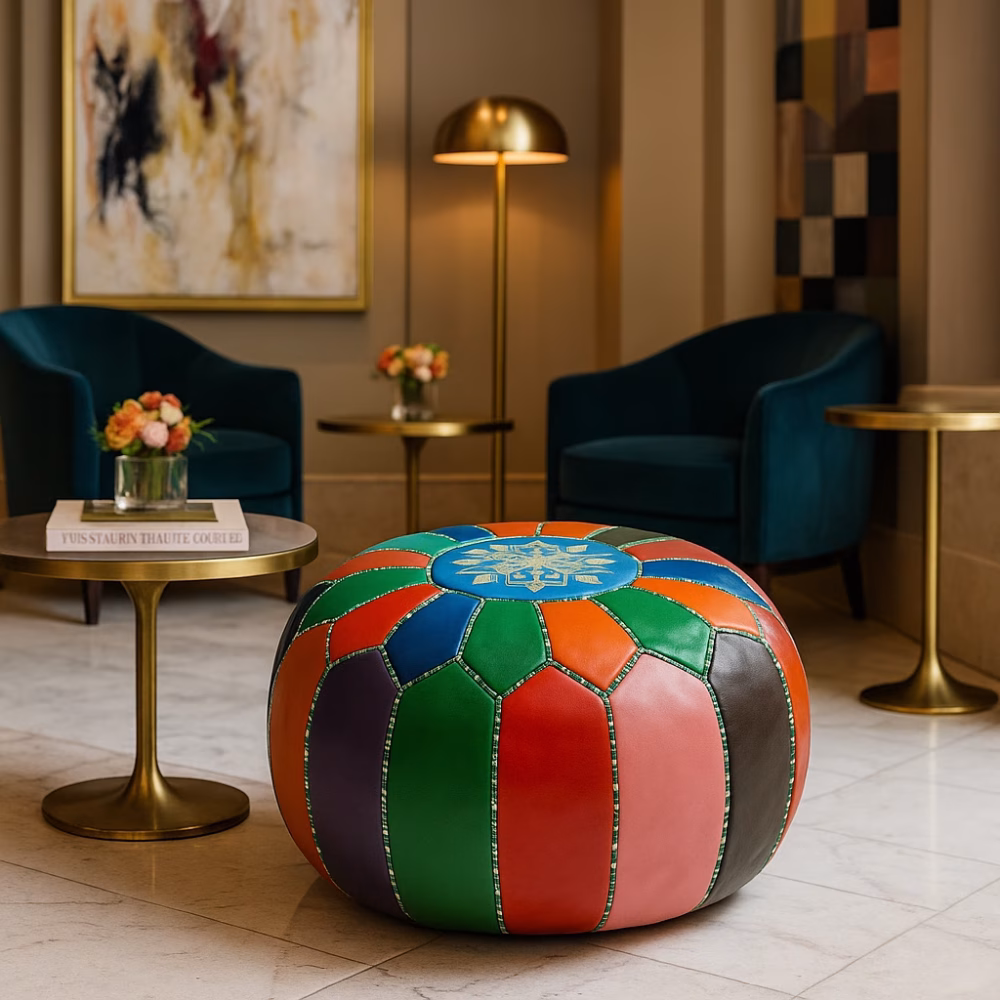 A vibrant leather pouf ottoman with multicolor patchwork design in a modern hotel lobby with teal chairs and gold accents.