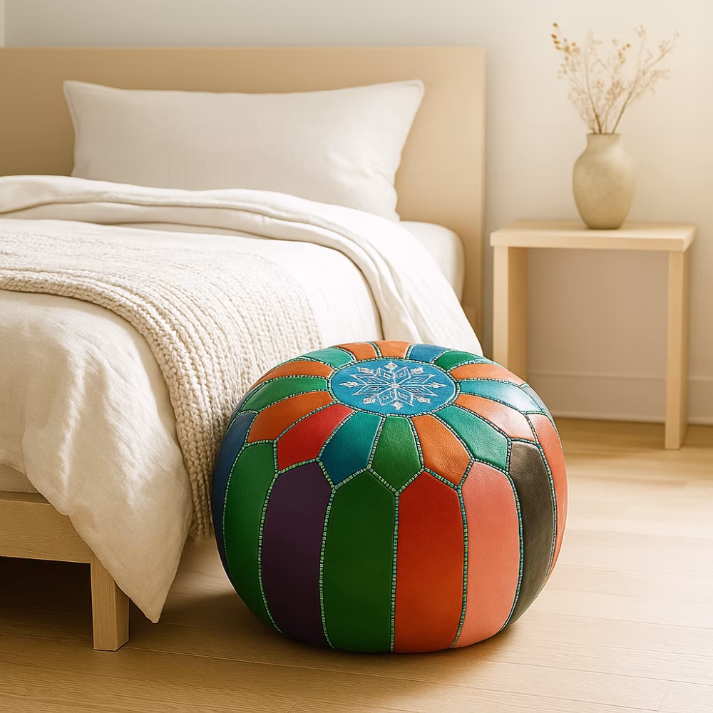 Colorful leather pouf ottoman placed at the foot of a minimalist bed in a bright, modern bedroom.