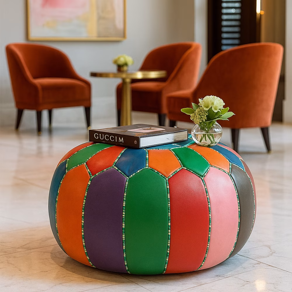 Colorful leather pouf ottoman used as a stylish centerpiece in a hotel lounge with orange chairs and marble floors.