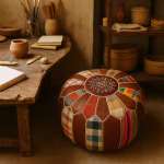 Colorful round leather pouf ottoman with patchwork panels in a rustic artisan studio setting.