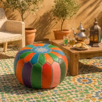 Multicolored leather pouf ottoman on a Moroccan mosaic-tiled terrace next to traditional tea and lantern decor.