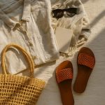 Flat-lay of light-brown Leather Slides styled with linen shirt, straw tote, and sunglasses for a beach-day look.