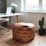 Square leather floor pouf near window in home office, portable cognac cube ottoman with geometric stitching
